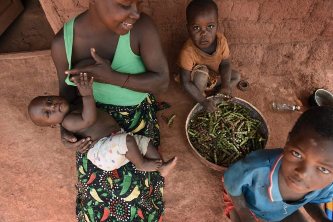 Een Mozambikaanse vrouw zit samen met haar drie kinderen voor haar huis